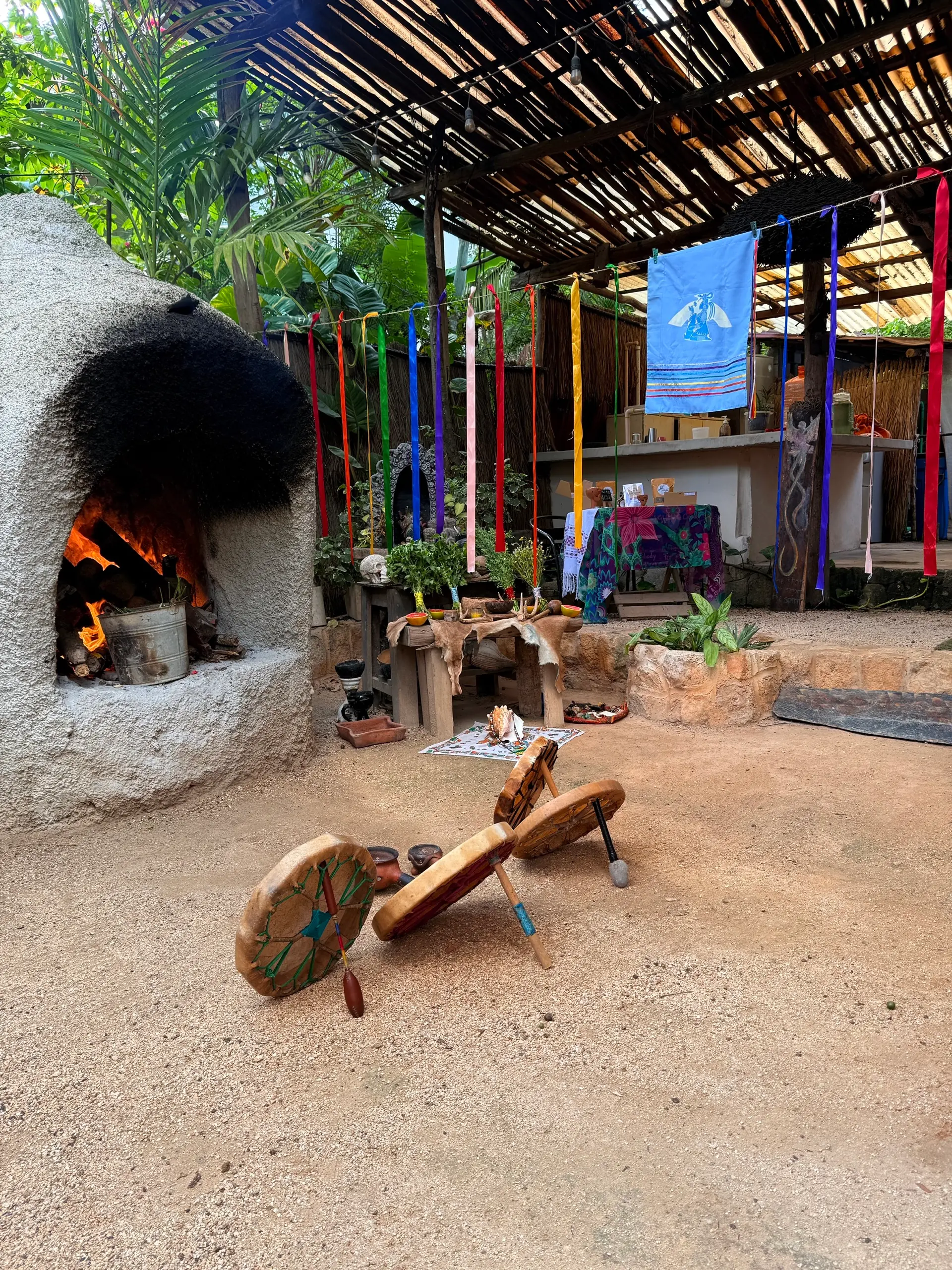 The stone oven burning, with the seven-colour ribbons on either side and the drums on the ground